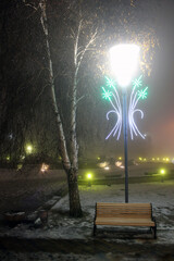 Wall Mural - Glowing lantern at night above a wooden bench in winter