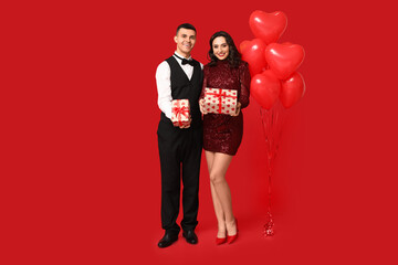 Canvas Print - Loving young couple with heart-shaped balloons and gift boxes on red background. Celebration of Saint Valentine's Day