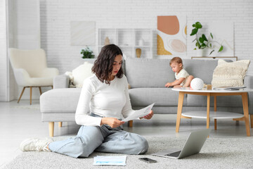 Canvas Print - Cute little baby and young mother working with laptop while reading documents on maternity leave at home