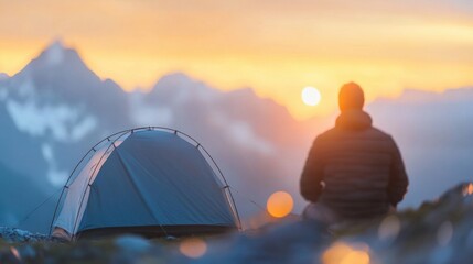 Wall Mural - a man sits peacefully outside his tent, taking in the stunning mountain view as the sun sets, surrou
