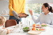 © Pixel-Shot - Young man putting Fajita on table at dinner with his family in kitchen