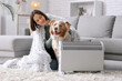 © Pixel-Shot - Young woman with blanket and Australian Shepherd dog sitting near heater at home