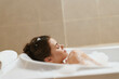 © SHOTPRIME STUDIO - Relaxed young woman enjoying a soothing bubble bath in a modern bathroom, surrounded by soft light and calming colors for a peaceful atmosphere.