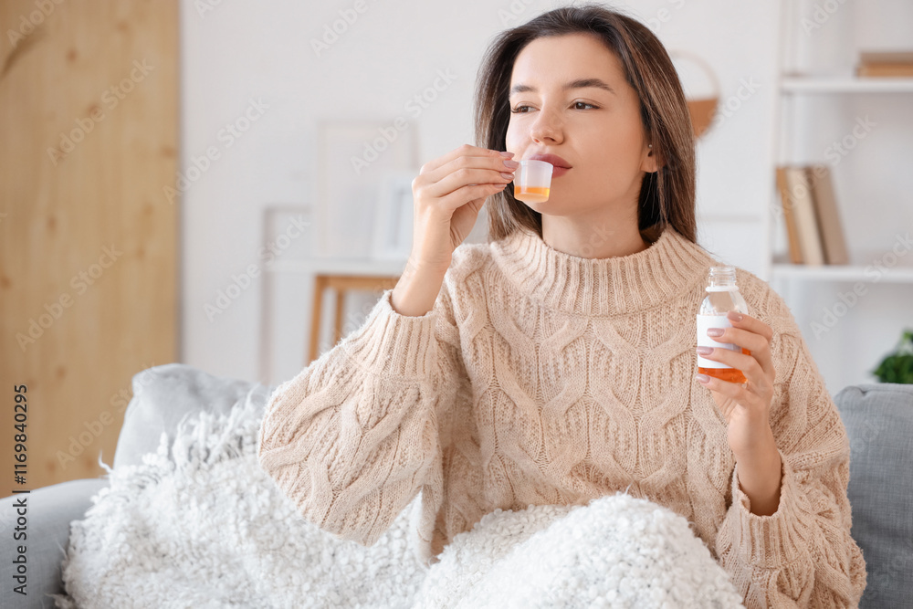 Sick young woman taking cough syrup on sofa at home