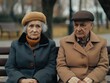 © vefimov - An elderly couple sitting side by side on a park bench, dressed in warm clothing against the winter chill. They appear to be engaged in a quiet conversation or lost in thought.