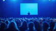 © Planetz - Large Crowd of People at an Event Featuring One Person on Stage in a Dimly Lit Environment with a Projector Screen in the Background