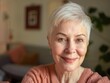 © Alexandr - Woman with short gray hair, smiling warmly for the camera, in a comfortable indoor home setting.