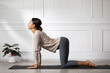 © 220 Selfmade studio - Asian young woman performing the cat-cow yoga pose on a mat in a bright, minimalist indoor setting