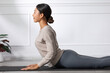 © 220 Selfmade studio - Asian young woman performing the cobra pose during a yoga session on a mat in a bright, minimalist indoor space. She exudes calmness and focus