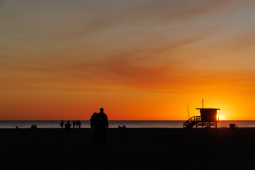 Fototapete - Los Angeles beach at sunset, featuring a lifeguard tower silhouette against a glowing orange and purple horizon