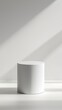 © Vidobe - Minimalist white cylinder podium on white floor with sunlight.