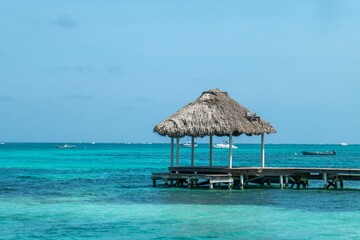 Poster - Tropical beach scene with a thatched-roof hut over turquoise waters.