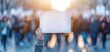 © Suhainee - A blurred crowd protests in sunlight, with a hand displaying a blank sign, symbolizing voicing opinions and demands.