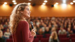 © Bonsales - Young woman holding microphone and giving presentation in crowded auditorium, sharing her expertise with enthusiastic listeners