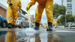 © Kannika - Cholera prevention. Workers in yellow rain gear cleaning a flooded street with a broom.