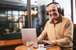 © inesbazdar - Smiling senior man in casual clothing with wireless headphones using laptop and drinking coffee while sitting in the cafe.