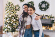© BullRun - Happy sisters hugging for photograph in room decorated for Christmas