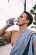 © BullRun - Handsome caucasian male jogger with slim figure drinking water after workout outdoors standing on street, young 20s gyt without t-shirt making pause for refreshment feeling thirsty