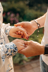 Wall Mural - Close-up photo of hands of bride and groom in love during wedding ceremony against the backdrop of flower arch in the sun