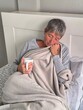 © AndreaMonica - Young sick woman under the covers with a cup in her hand.Woman wrapped in blanket sits in bed with a cup of coffee in her hands.Woman with a cup in her hand in bed under the covers depressed and sad.