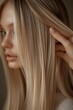 © Denis - Captivating close-up of a young woman styling her long, straight blonde hair indoors during soft afternoon light