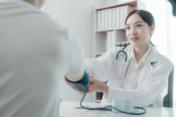 Young Asian nurse measures blood pressure of young man while they sit at table, medical health concept