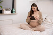 © fotodrobik - A pregnant woman using a tablet in a cozy, beautifully designed bedroom, feeling serene
