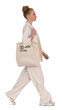 © Martin - Fashionable woman in a beige suit and carrying a tote bag walking in profile side towards the camera isolated on transparent background