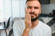 © Serhii - Dental health problems concept. Man suffering from strong toothache. Upset male patient with inflamed nerve, tooth abscess, or teeth sensitivity sitting on sofa and touching cheek with grimace of pain