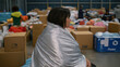© Vasiliy - Person covered with reflective blanket among donation boxes. Emergency shelter concept