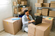 © AntonioDiaz - Small ecommerce business owner managing orders and talking with customers on the phone while working on a laptop in a small warehouse