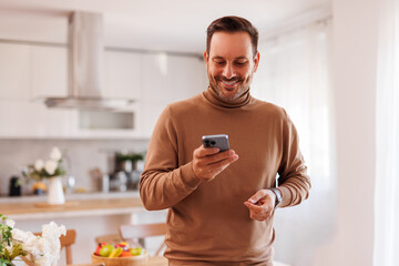 Wall Mural - Portrait of handsome entrepreneur smiling and using social media apps over mobile phone at home