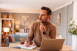 © Moon Safari - Portrait of serious male programmer thinking and writing in note pad while working over laptop at home