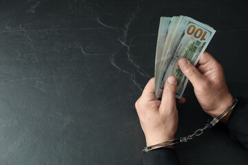 Wall Mural - Corruption. Man in handcuffs with dollar banknotes at grey textured table, closeup. Space for text