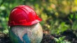 © thenort - Red hard hat on a small globe in soil, green background.