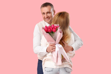 Wall Mural - Middle-aged couple with bouquet of flowers hugging on pink background. International Women's Day