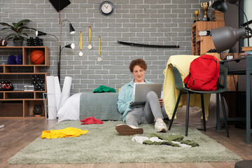 Wall Mural - Male student using laptop in messy bedroom