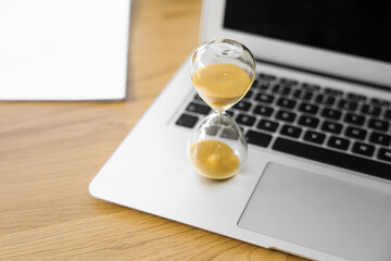 Wall Mural - Hourglass with laptop on desk in office, closeup