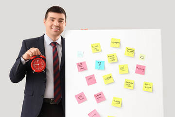 Wall Mural - Young businessman with alarm clock and sticky notes on light background. Time management concept