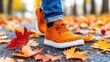© kamonrat - Bright orange sneakers stand out among fallen autumn leaves on a paved path. A person wearing rolled-up jeans walks through the colorful, crisp foliage, capturing the essence of fall
