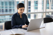 © fizkes - Positive busy young Indian businesswoman typing on laptop in office, sitting at workplace table with large window behind, working on online project, using technology for job communication