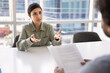 © fizkes - Serious beautiful young businesswoman talking to male business colleague at meeting table, speaking at job interview, consulting legal advisor, lawyer holding paper document