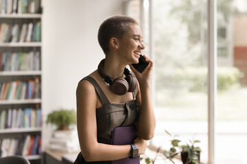 Wall Mural - Smiling millennial trendy looking female hipster saleswoman at bookstore librarian stand by window calling by phone consult customer about new books answer reader questions about lending library price