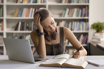 Wall Mural - Writing essay. Focused left handed female teenager highschooler student prepare for lectures at campus library take brief notes of paper monograph book use notebook pc to get more information online