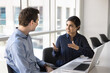 © fizkes - Happy positive young Indian businesswoman discussing project plan with male colleague. Diverse couple of coworkers brainstorming on startup ideas at workplace, talking at laptop