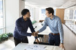 © fizkes - Cheerful young African businessman shaking hands with Caucasian business partner at work table, closing deal, getting agreement after analyzing project marketing sales reports