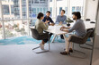 © fizkes - Diverse team of young male colleagues listening to speaking Indian business leader at meeting table in collaboration room interior, talking in contemporary workspace. Candid shot with copy space