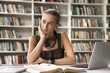 © fizkes - Difficult task. Thoughtful bored hipster teen female student sit at library desk by notebook propping cheek with hand feel tired of monotonous paperwork dull studies overworked preparing for hard exam