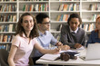 © fizkes - Diligent student. Portrait pretty teenage girl successful high school learner smart college pupil sit at library desk take part in group training with multiethnic teammates look at camera with smile