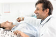 © fizkes - Happy endocrinologist doctor examining patients thyroid for nodes, disease, using modern ultrasound scanner, watching scanning result, smiling, laughing, sharing good news about checkup with man